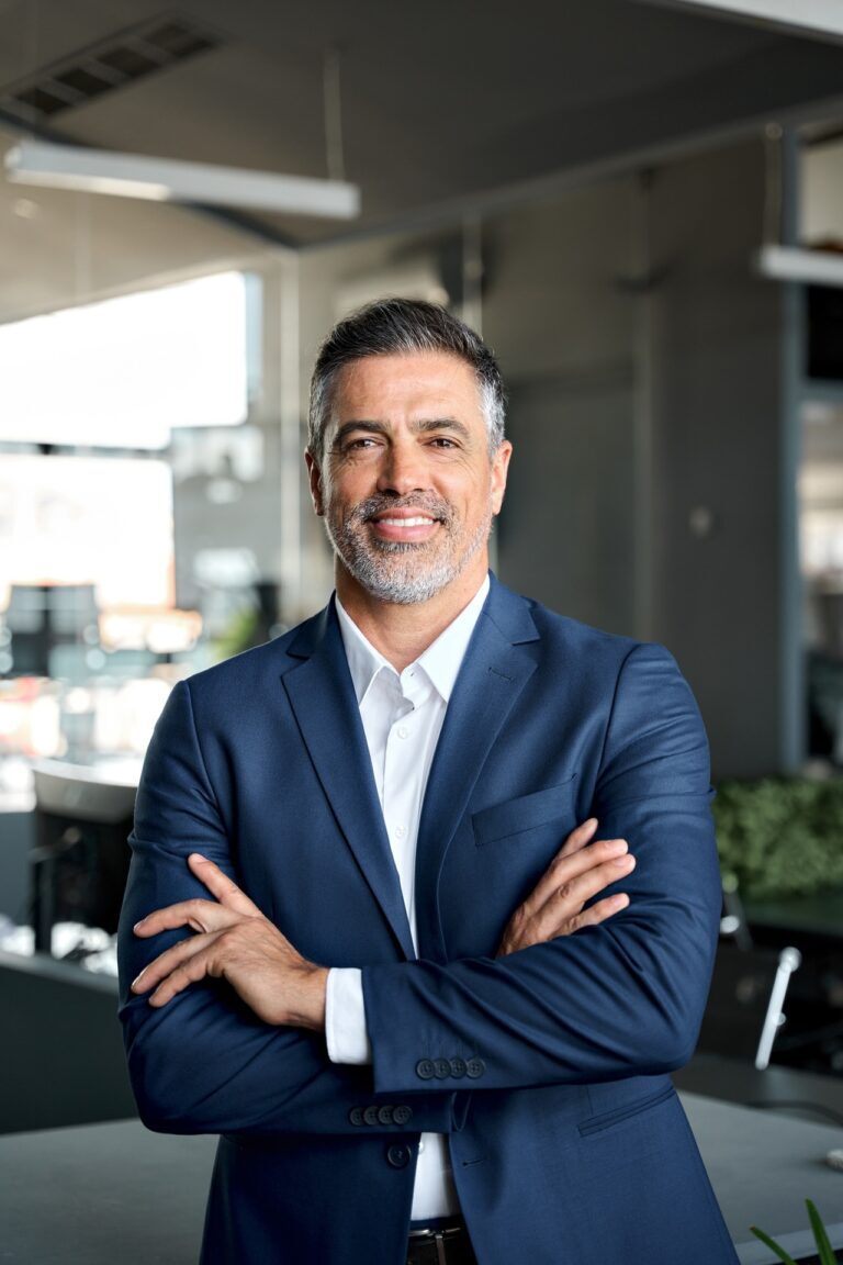 Smiling man in a blue suit stands with arms crossed, embodying executive professional presence.